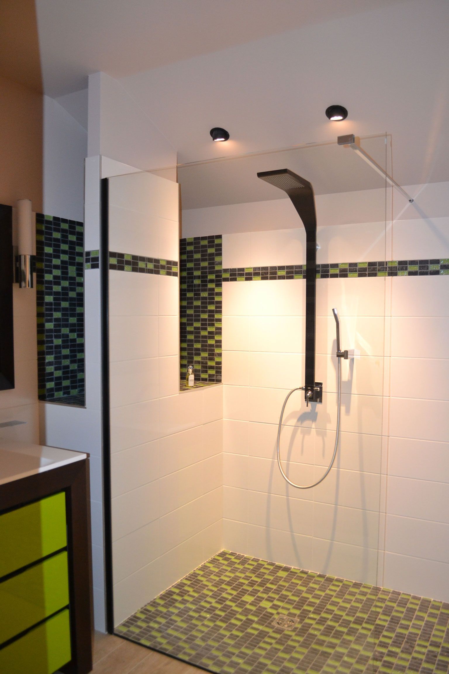 Cabine de douche moderne avec robinetterie noire, accents de mosaïque et paroi en verre.
