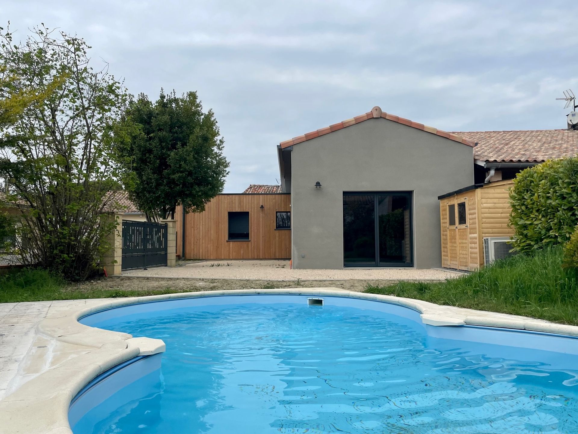 Jardin avec piscine devant une maison moderne ; un petit abri en bois est visible sur la droite.