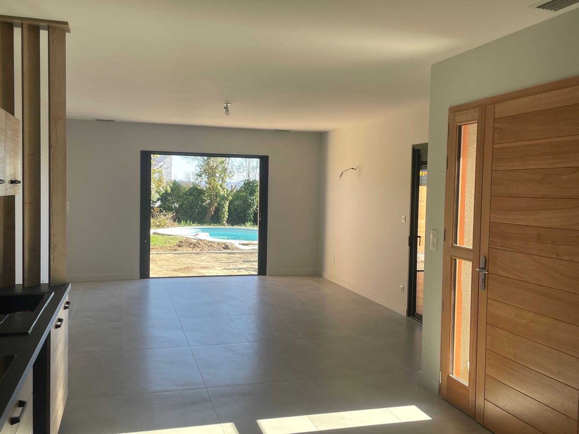Vue intérieure d'une maison moderne avec porte ouverte donnant sur un jardin avec piscine.