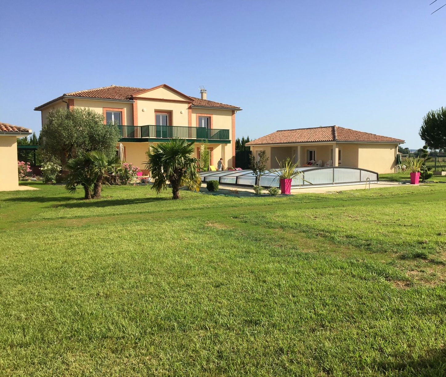 Une maison beige à deux étages avec des accents de brique, une véranda vitrée attenante et un ciel gris couvert.