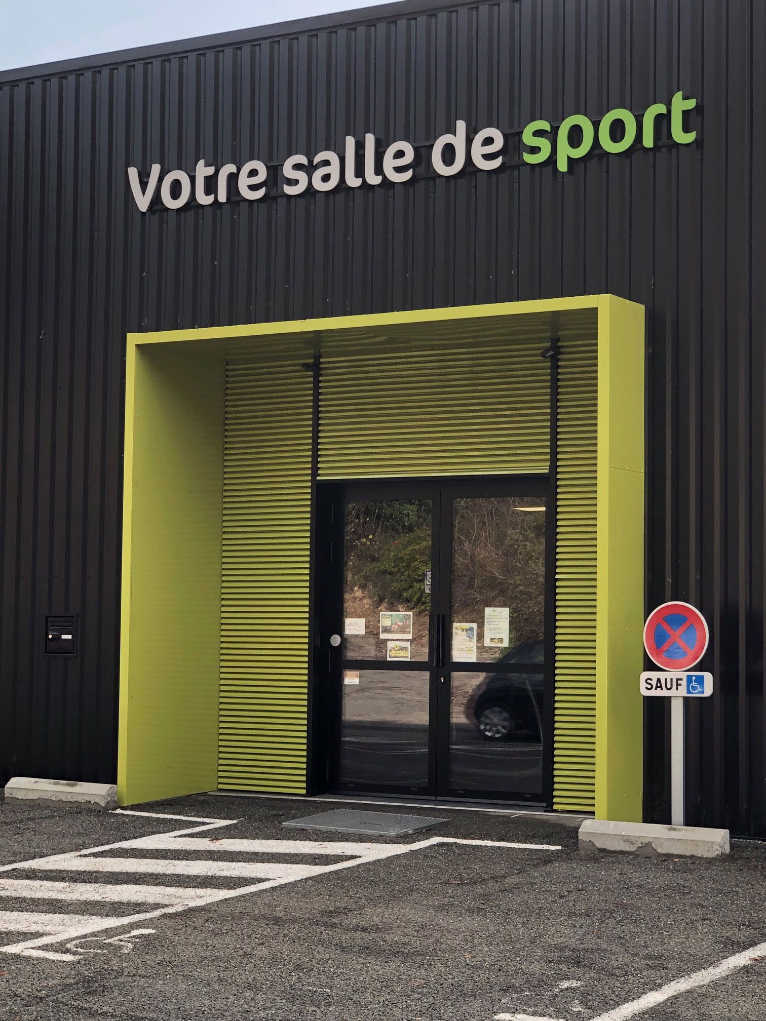 Entrée d'une salle de sport. Bâtiment noir avec un encadrement d'entrée vert et l'inscription Votre salle de sport.