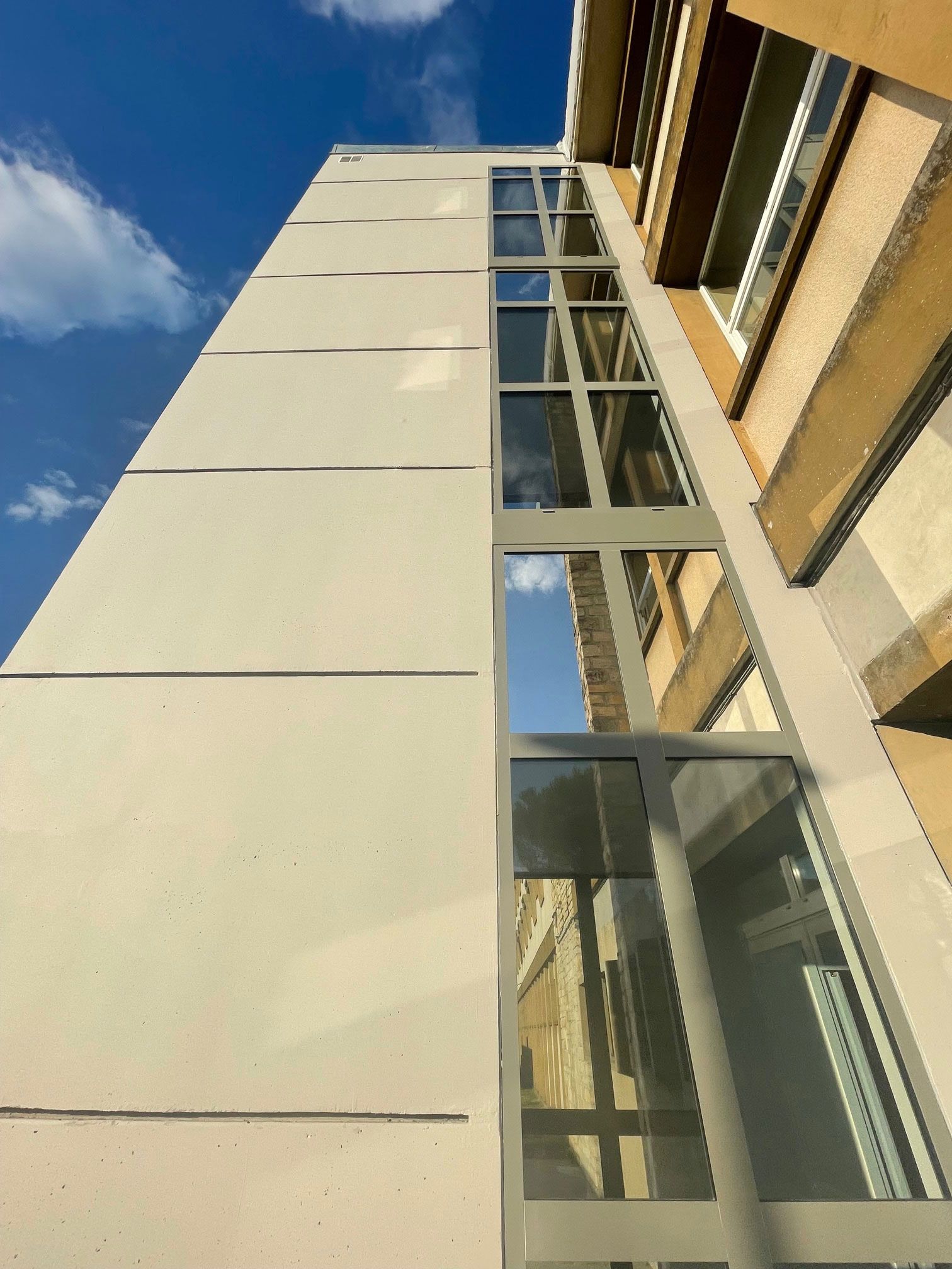 Immeuble de grande hauteur avec ascenseur vitré se détachant sur un ciel bleu. La façade est gris clair.