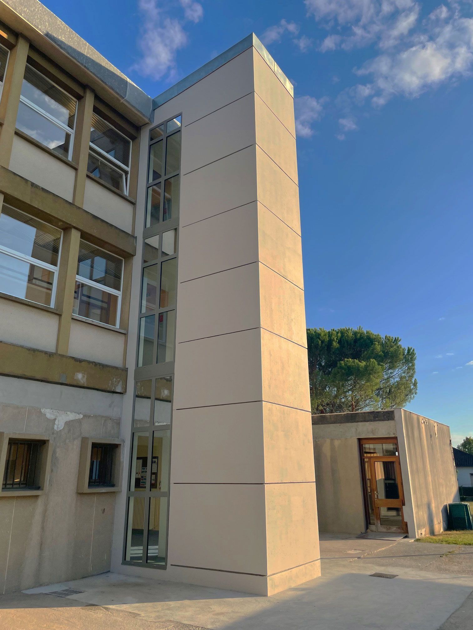 Extérieur d'un bâtiment avec une nouvelle cage d'ascenseur sur la droite. Ciel bleu en arrière-plan.