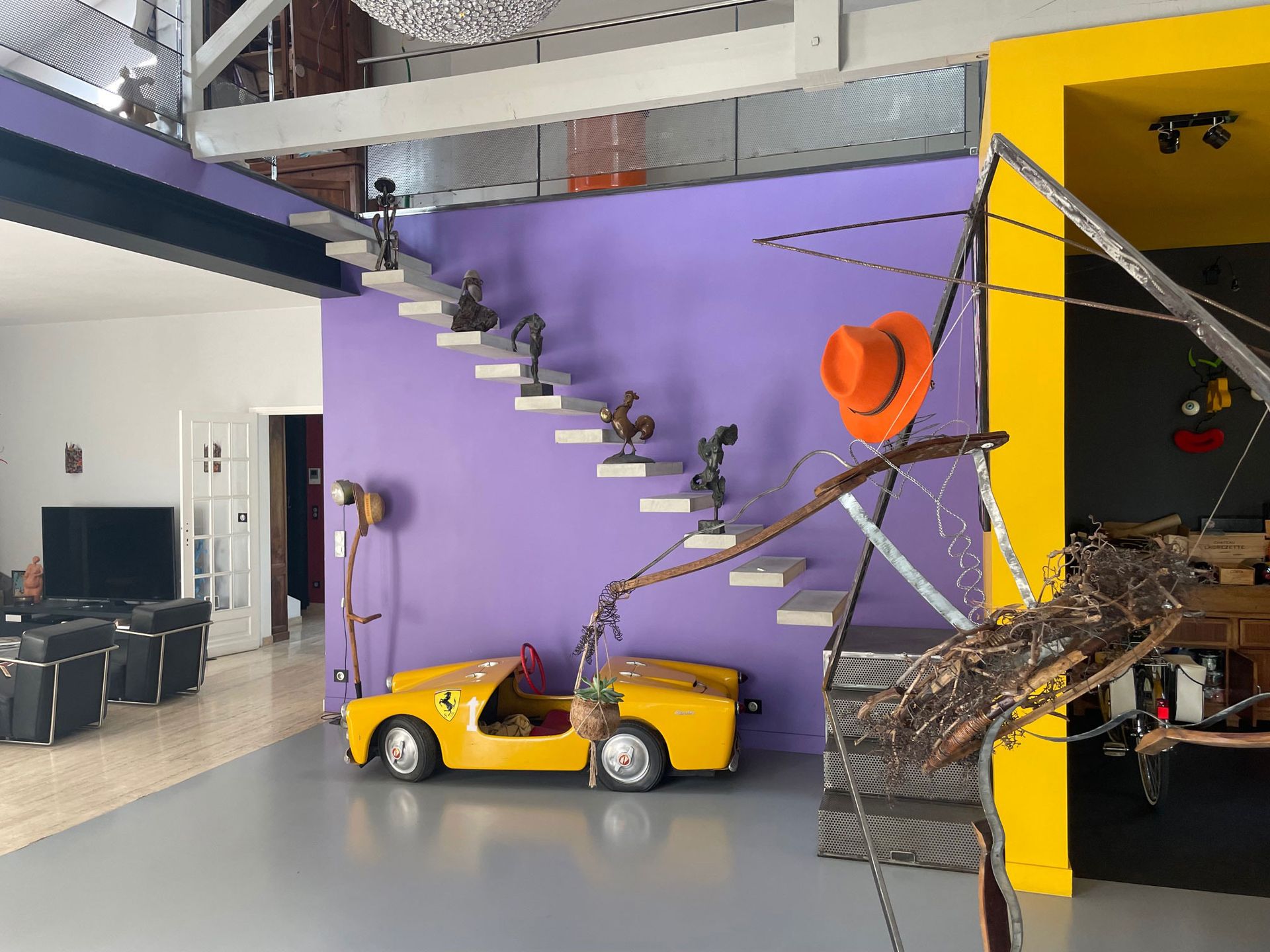 Voiture miniature jaune au pied d'un escalier violet orné d'installations artistiques.