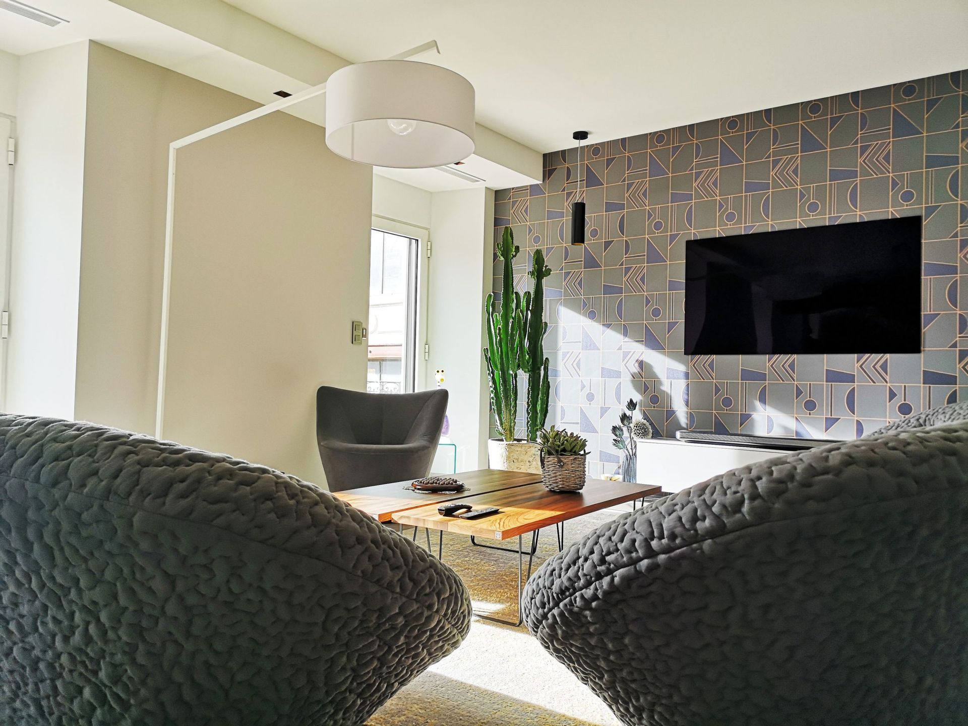 Salon avec mur d'accent texturé, télévision, fauteuils gris et table basse.