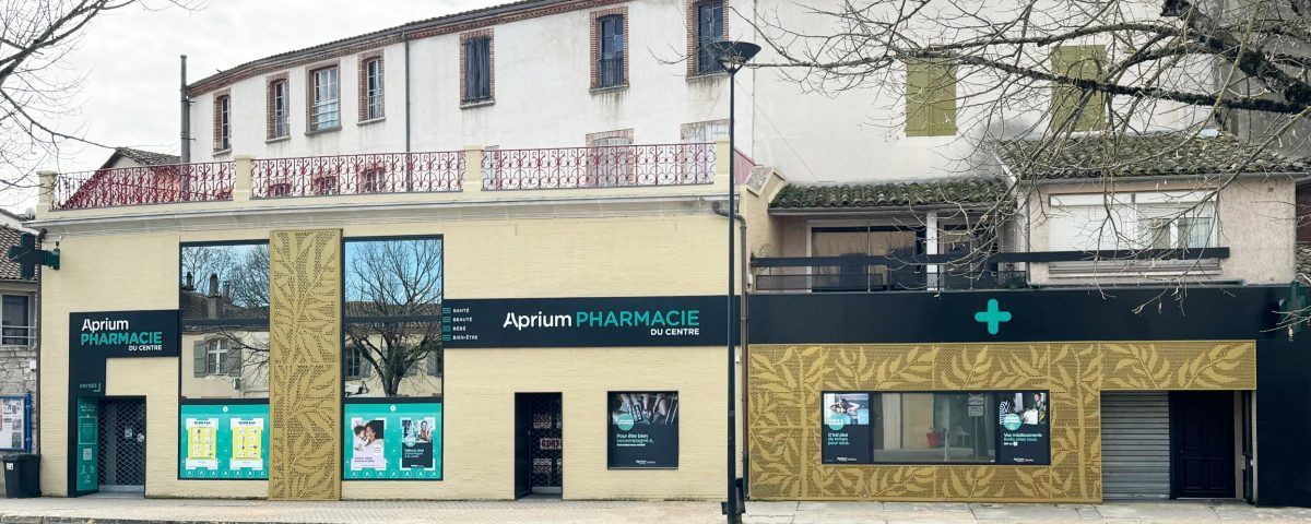Vue extérieure d'une pharmacie avec une façade beige et une croix verte.