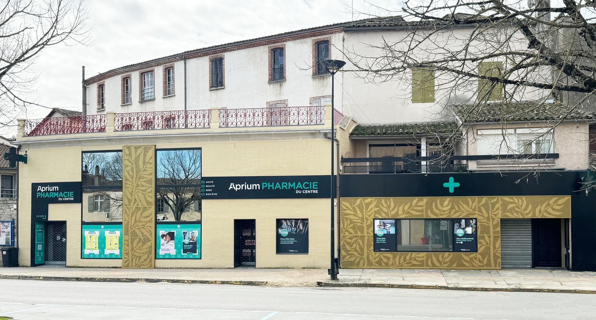 Extérieur d'un bâtiment moderne orné de graphismes et d'enseignes. Au-dessus, un immeuble ancien de plusieurs étages. Un arbre se dresse au premier plan.