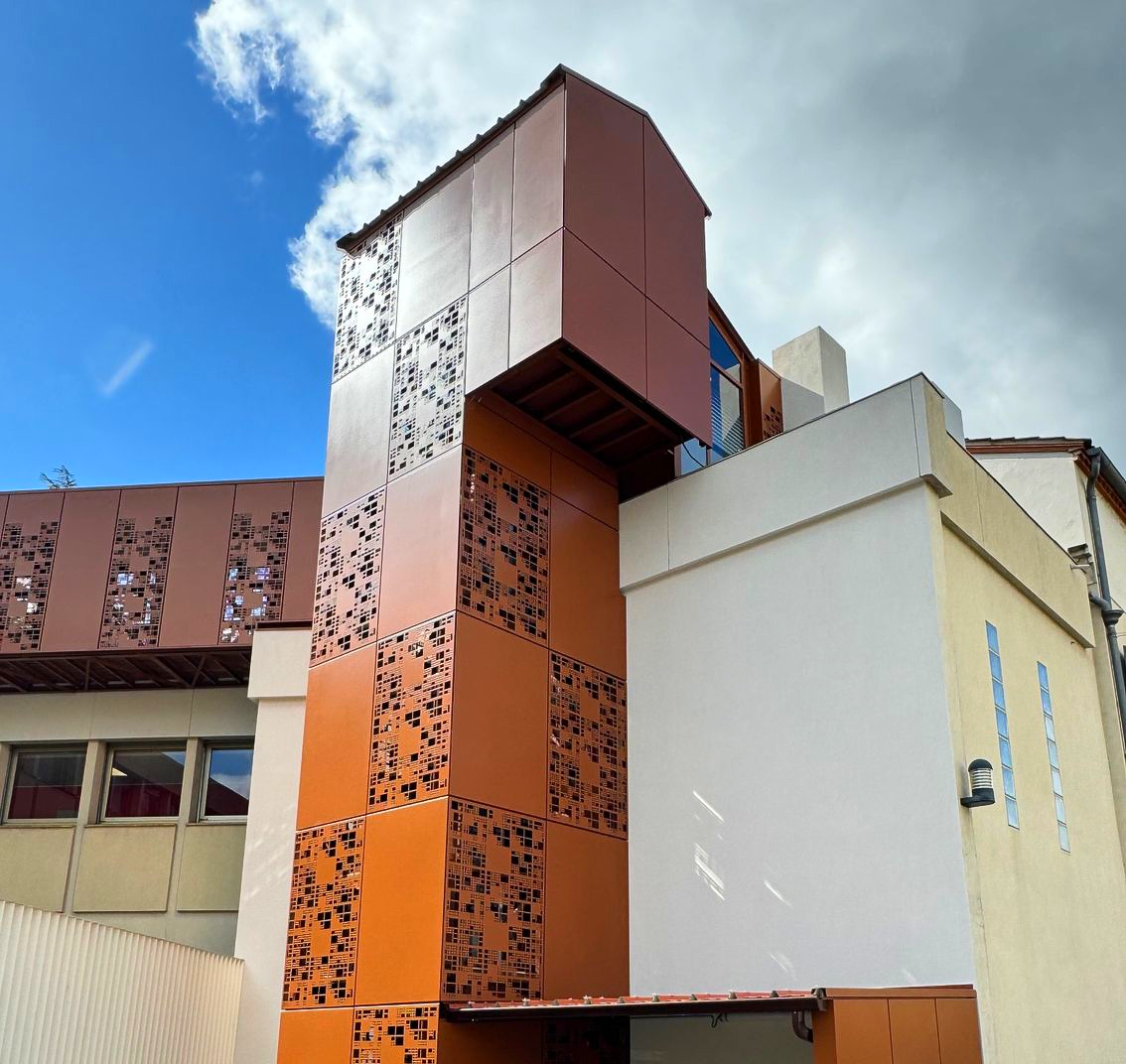 Bâtiment à façade métallique orange et panneaux perforés sous un ciel bleu.