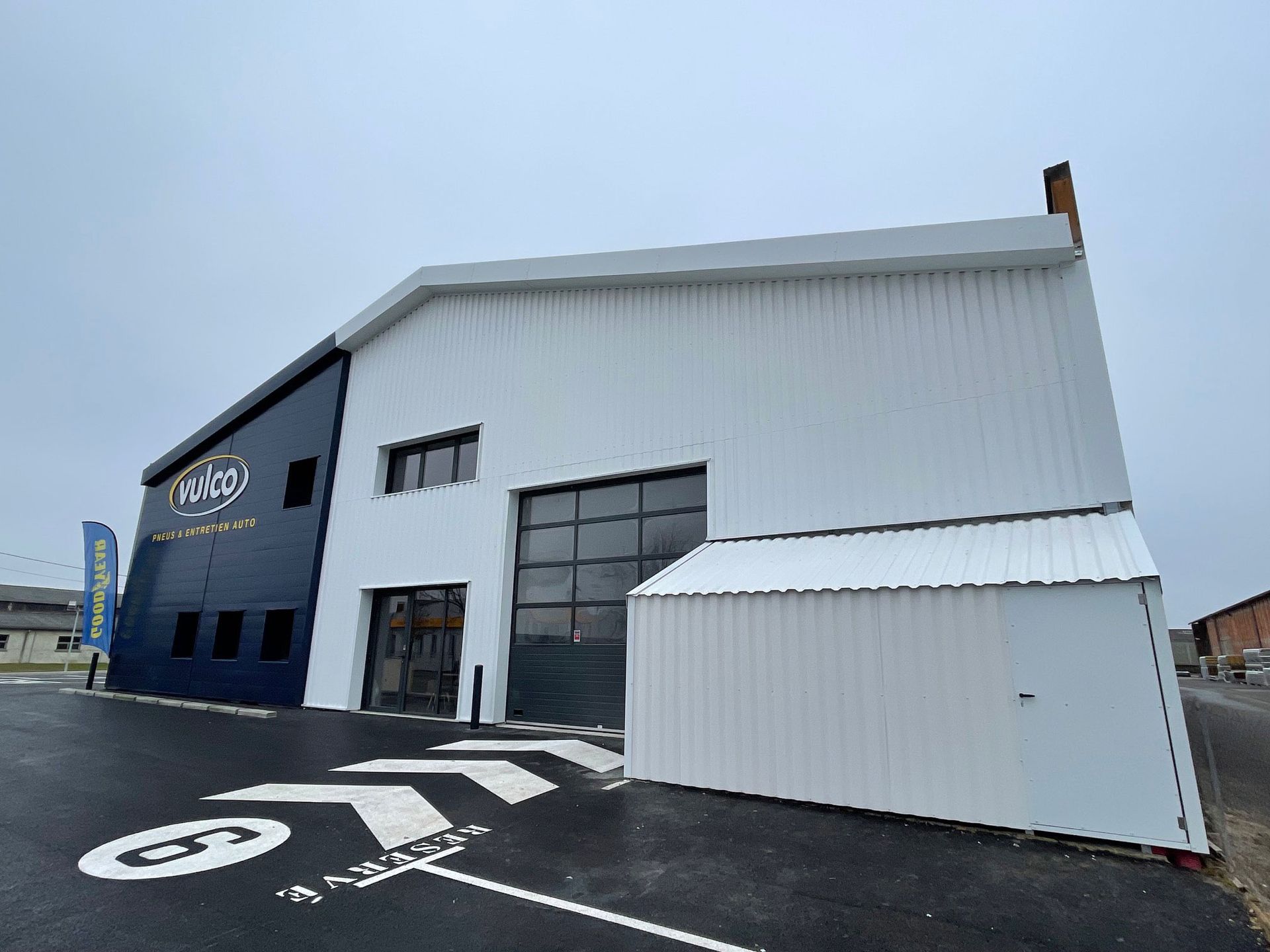 Vue extérieure d'un bâtiment moderne blanc et bleu foncé avec une grande porte de garage sur un terrain pavé.