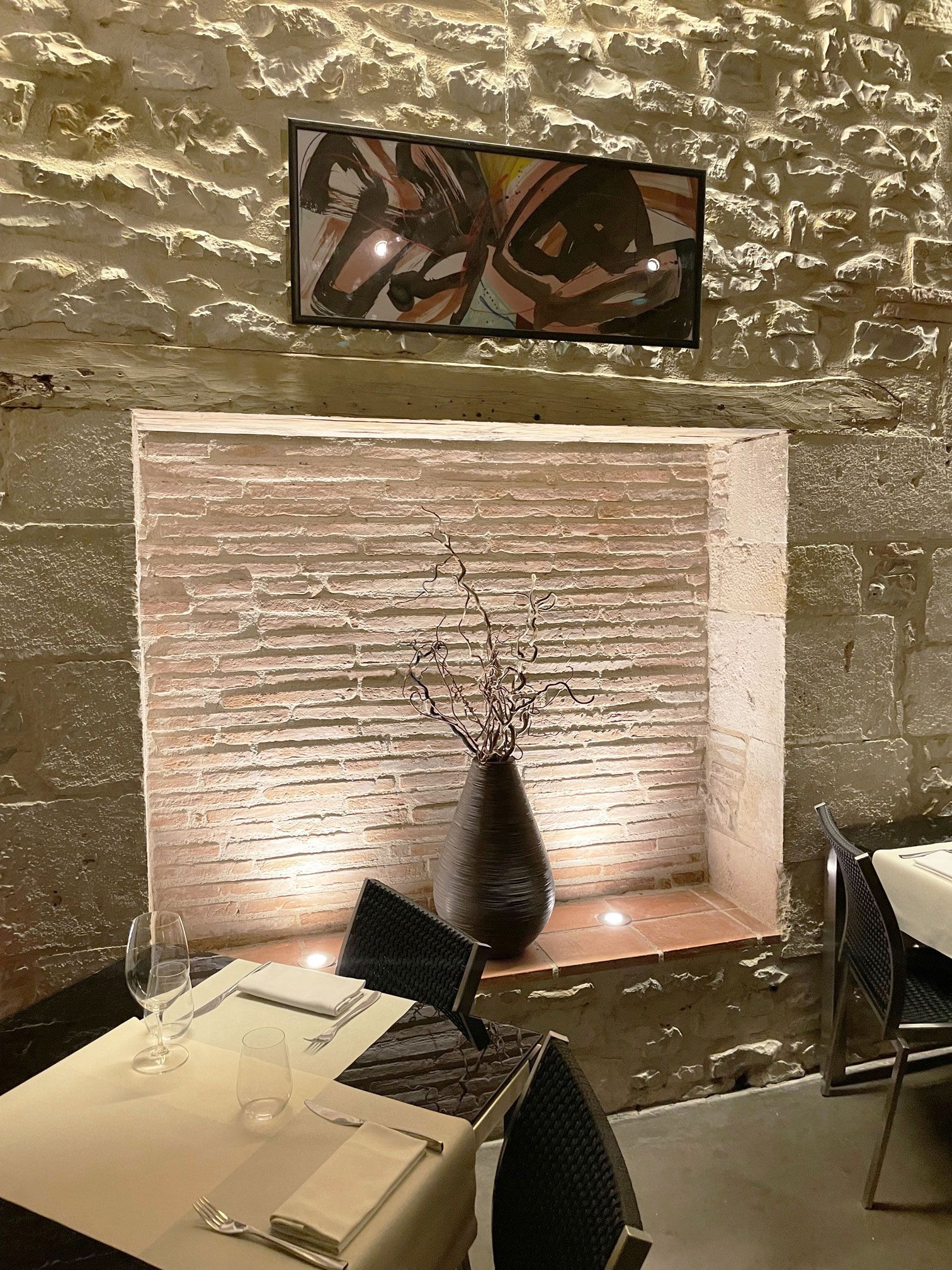 Intérieur d'un restaurant avec alcôve décorative, vase de branches, œuvres d'art et tables dressées pour le repas.