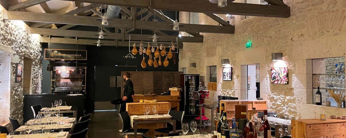 Intérieur d'un restaurant avec poutres apparentes et éclairage décoratif. On aperçoit des clients et des plats/boissons.