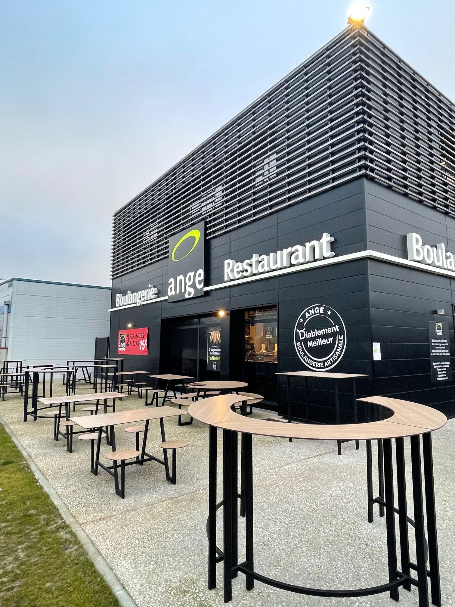 Extérieur d'un restaurant noir moderne avec tables en terrasse.