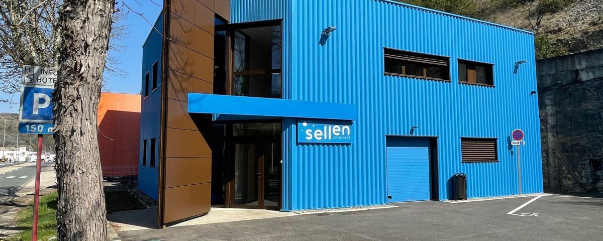 Bâtiment bleu avec des touches de brun. Rue avec panneau de stationnement devant.