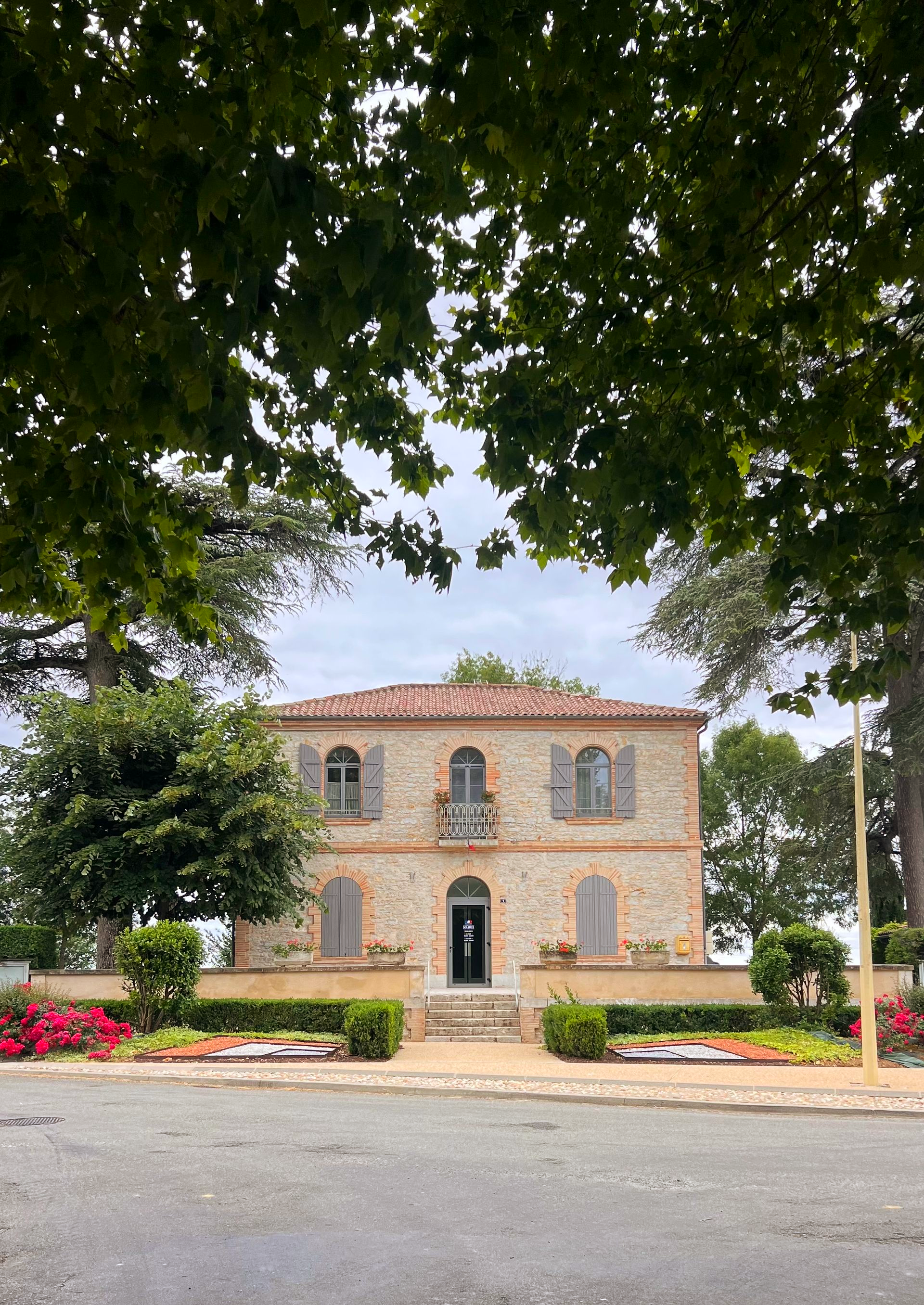 Un bâtiment en pierre encadré par des arbres, dans une rue bordée d'arbres.