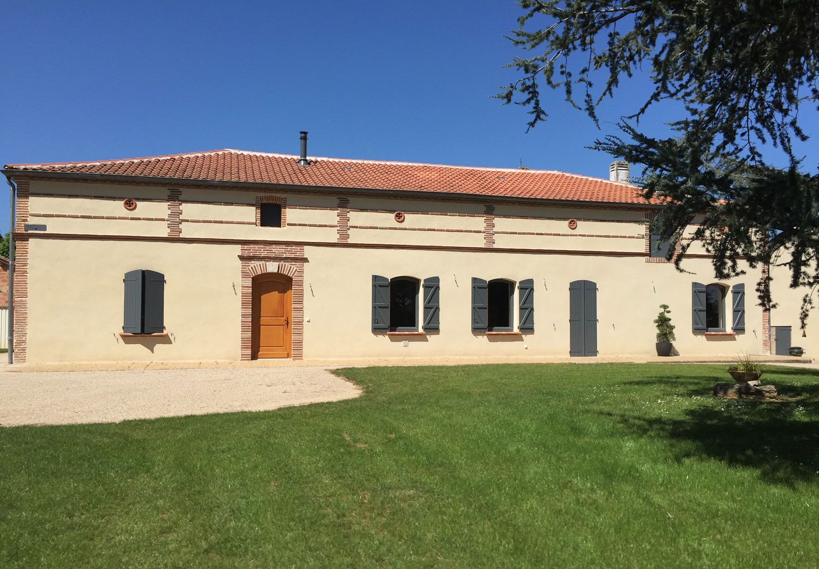 Maison beige au toit orange et à la pelouse verte par une journée ensoleillée.