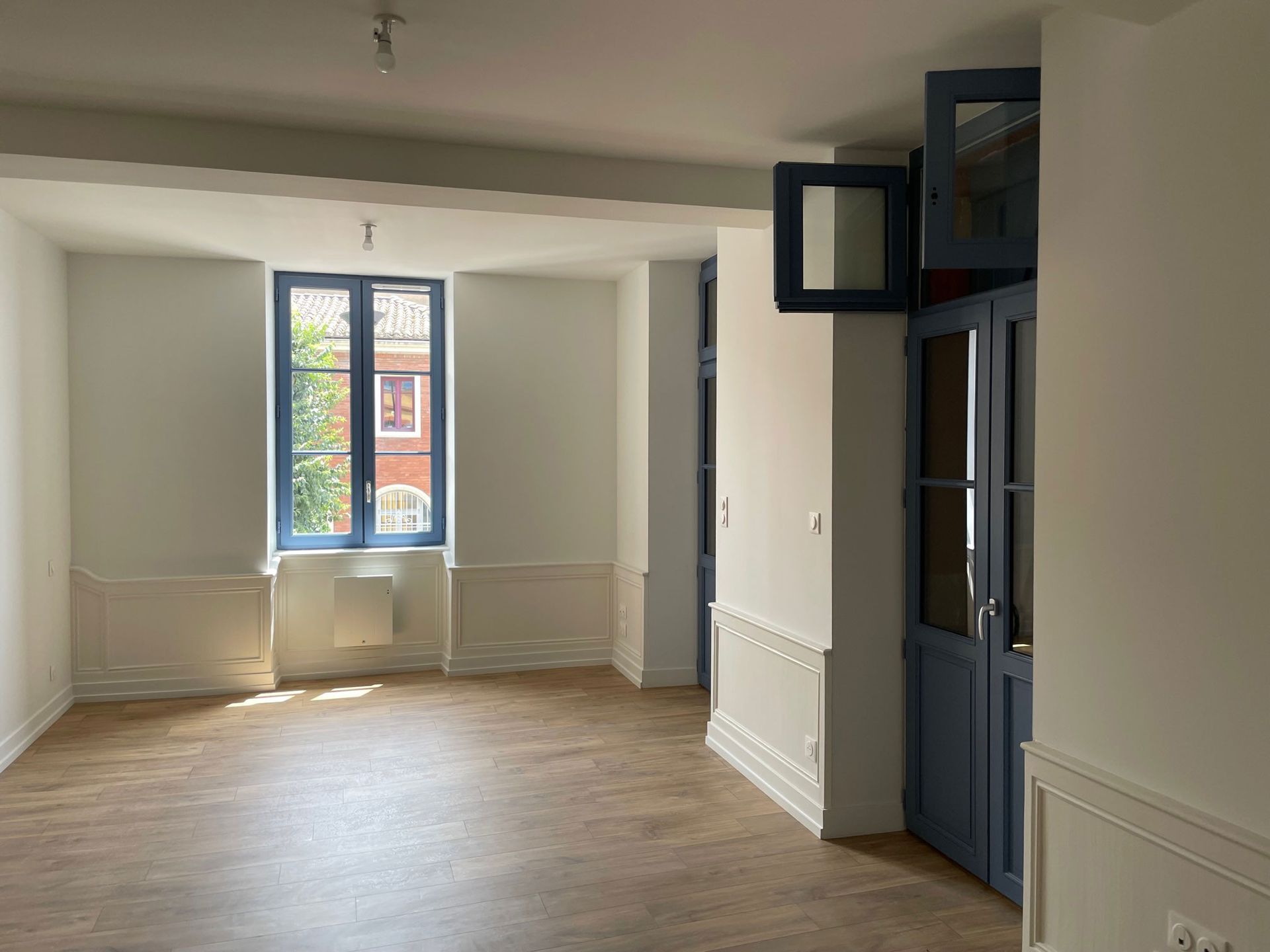 Pièce vide avec des encadrements de fenêtres et des portes bleus, des murs blancs et un sol imitation bois.