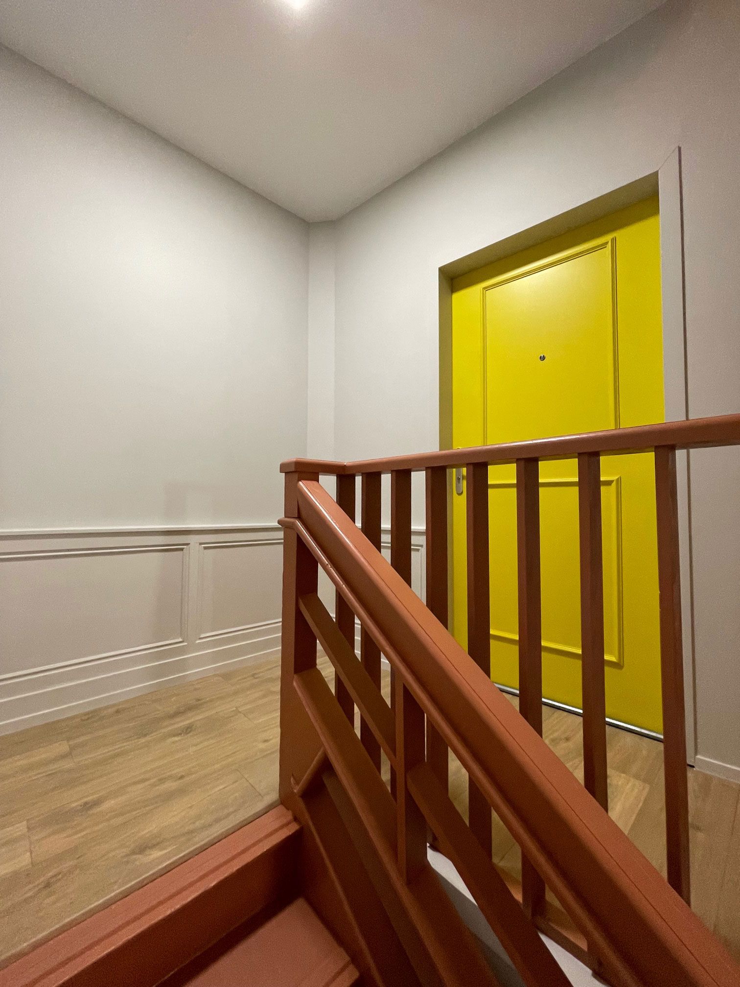 Un escalier en bois mène à une porte jaune vif. Des murs clairs entourent la cage d'escalier.