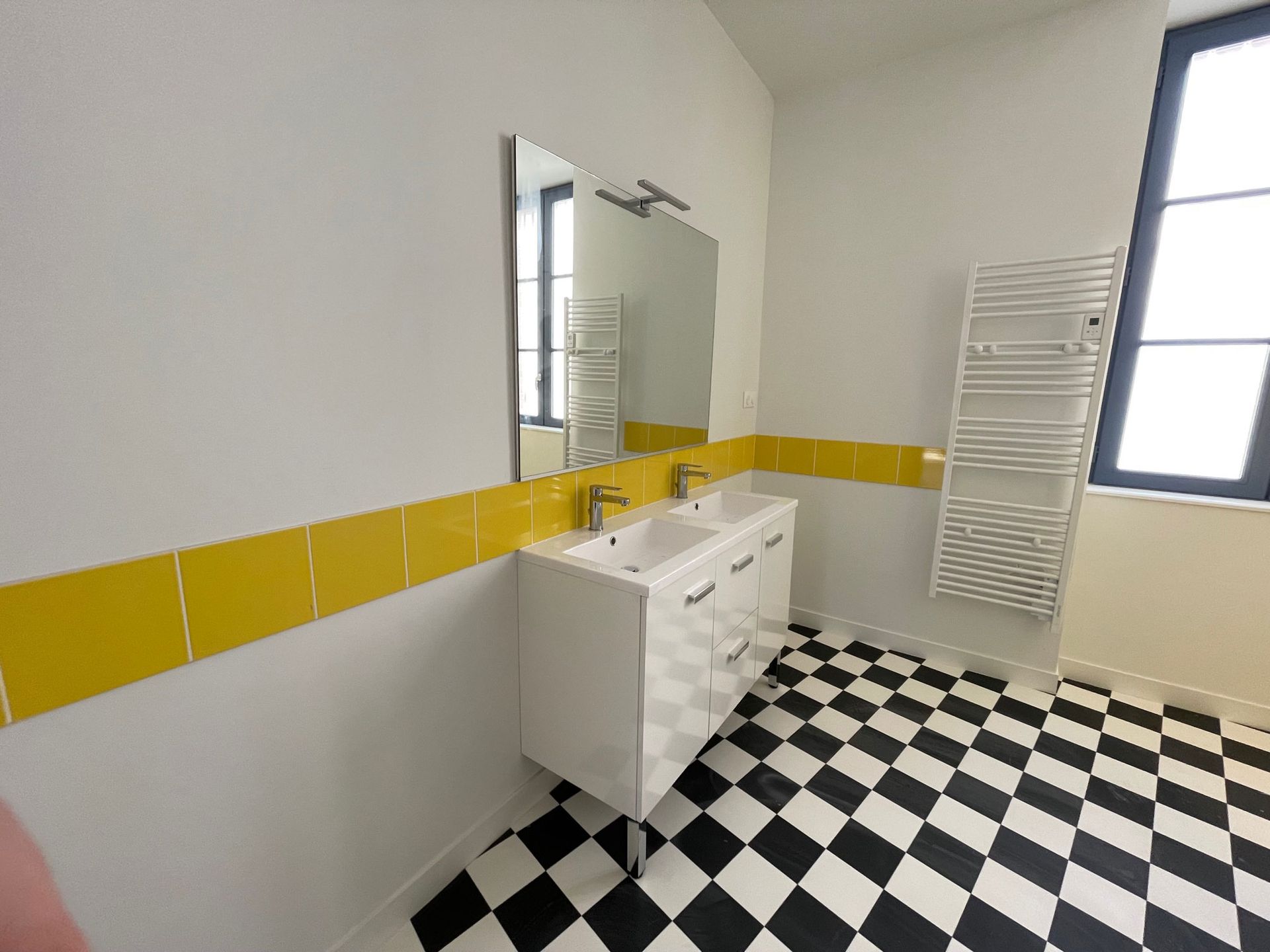 Salle de bains avec sol à damier noir et blanc, meuble-lavabo blanc et accents de carrelage jaune.