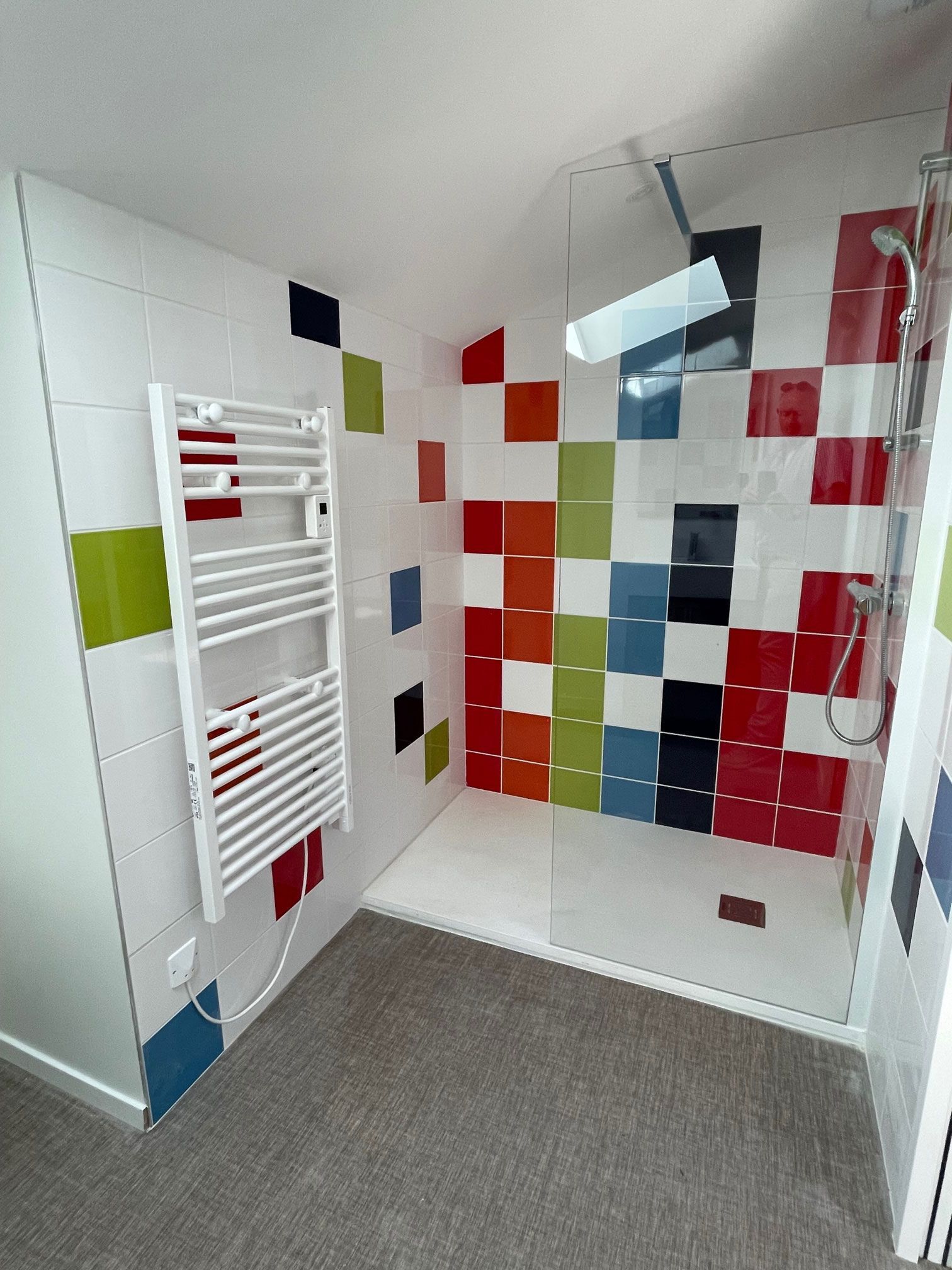 Douche carrelée colorée avec sèche-serviettes blanc.