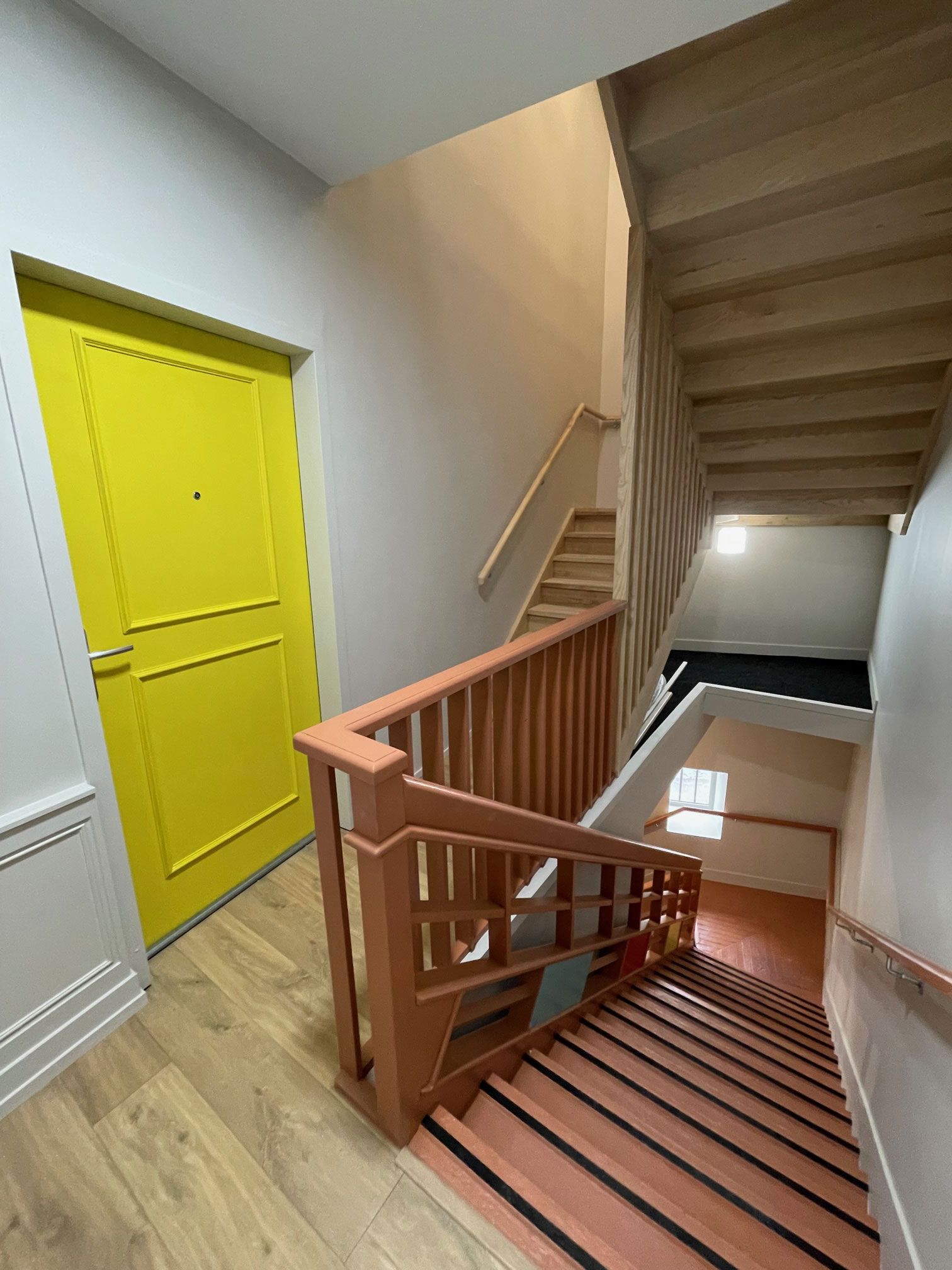 Porte jaune à côté d'un escalier avec rampe et marches en bois. Intérieur lumineux.