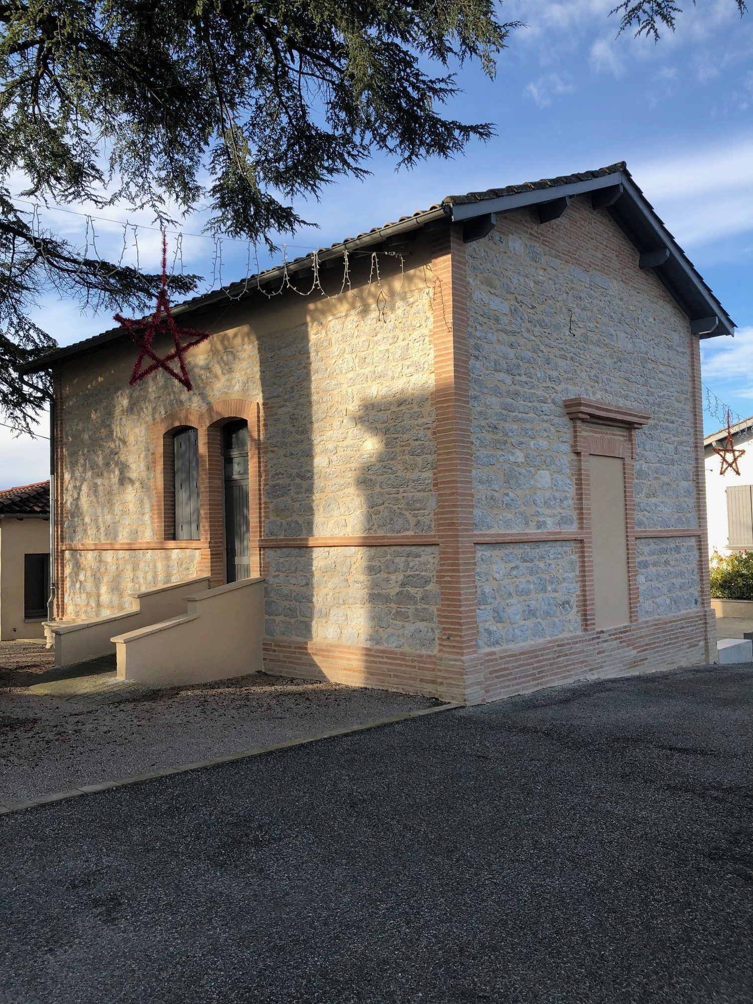 Petit bâtiment en pierre avec des accents de brique et une décoration en forme d'étoile rouge ; ciel bleu visible.