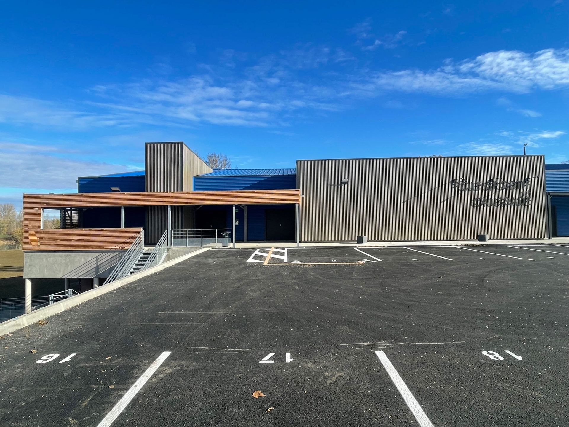Bâtiment à façade en bois rayée, toit bleu et parking sous un ciel bleu.