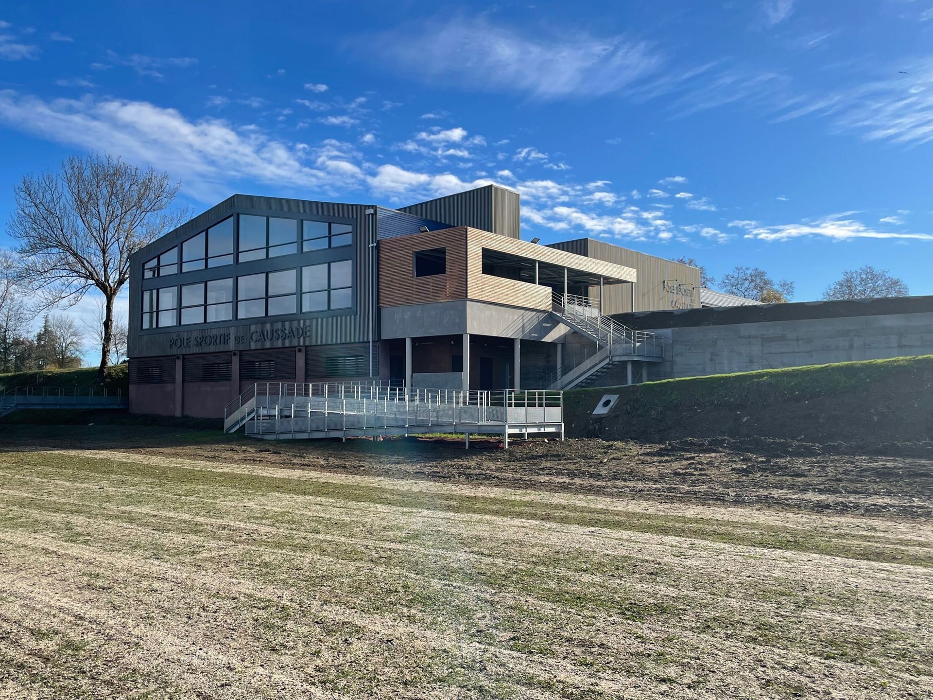 Bâtiment moderne avec de grandes fenêtres et une terrasse, sous un ciel partiellement nuageux.