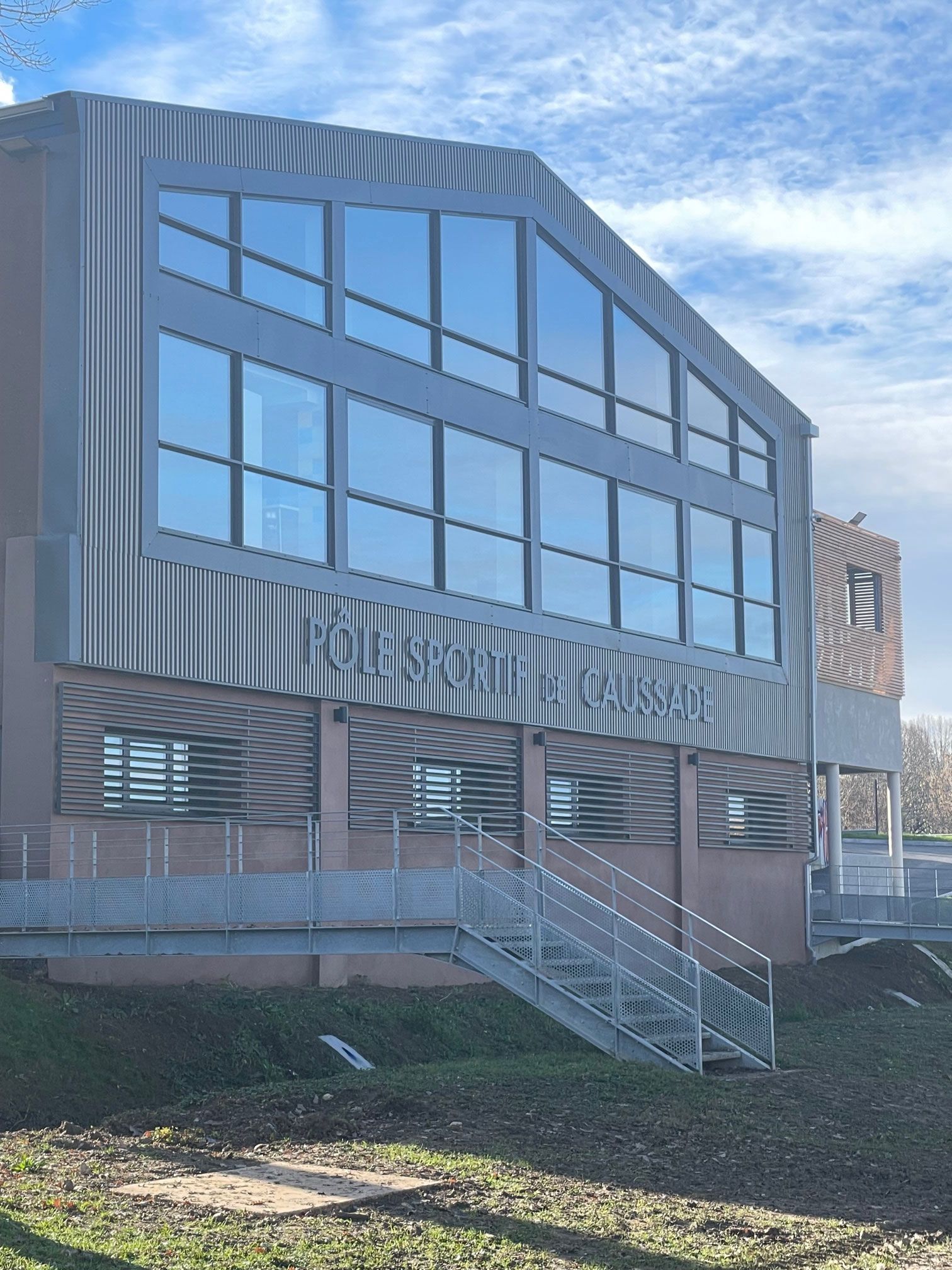 Bâtiment moderne avec de grandes fenêtres et une façade en métal, escalier menant à l'entrée.