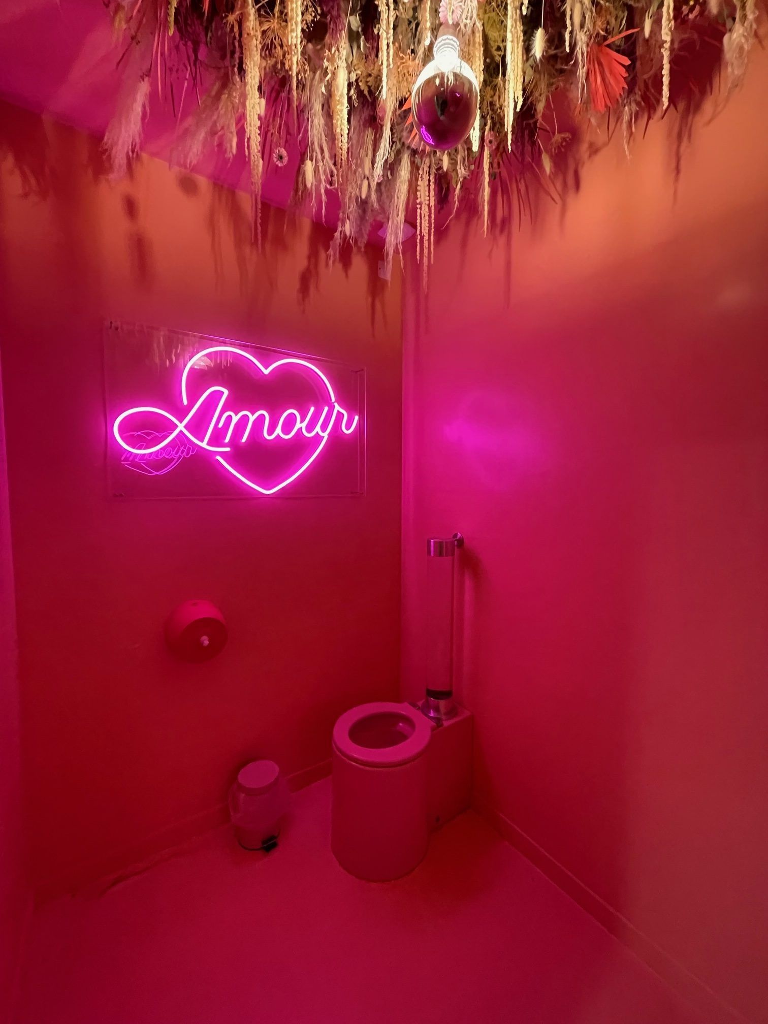 Toilettes roses avec enseigne lumineuse en forme de cœur Amour, plafond fleuri et WC.