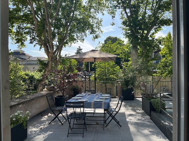 Un espace repas extérieur avec une table dressée, sous un grand parasol, entouré d'arbres.