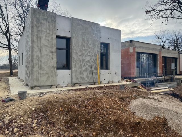 Maison miniature en construction d'après des plans architecturaux, avec de minuscules figurines au travail.