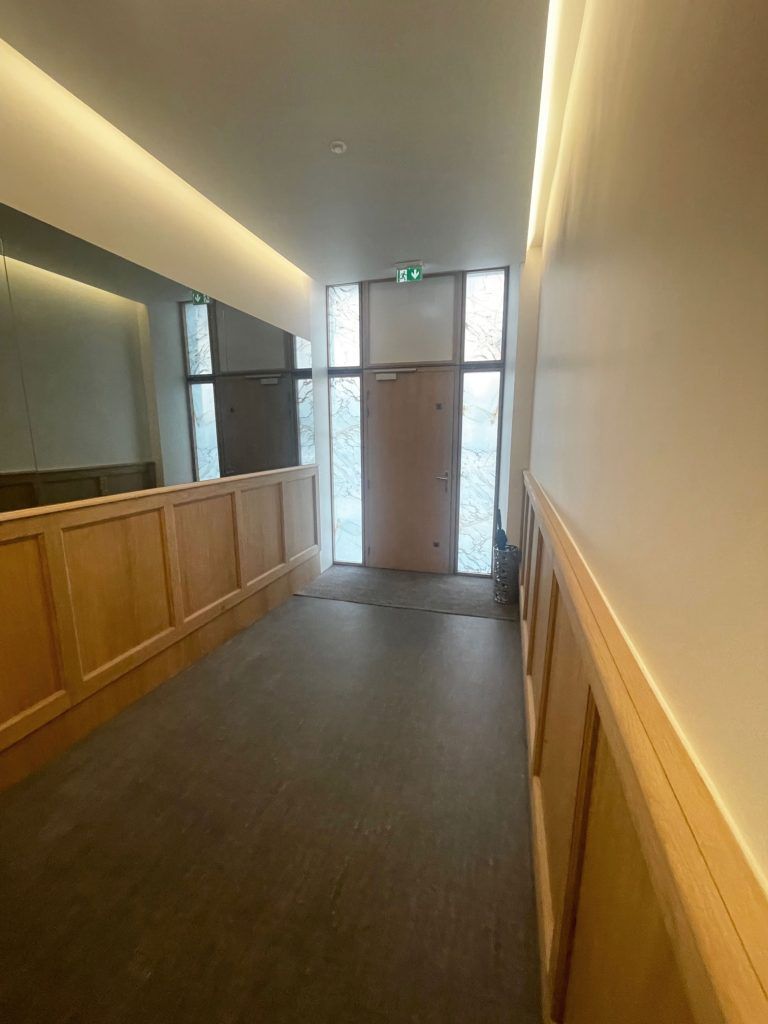 Couloir aux murs lambrissés bruns, une porte au fond et un plafonnier réfléchissant.