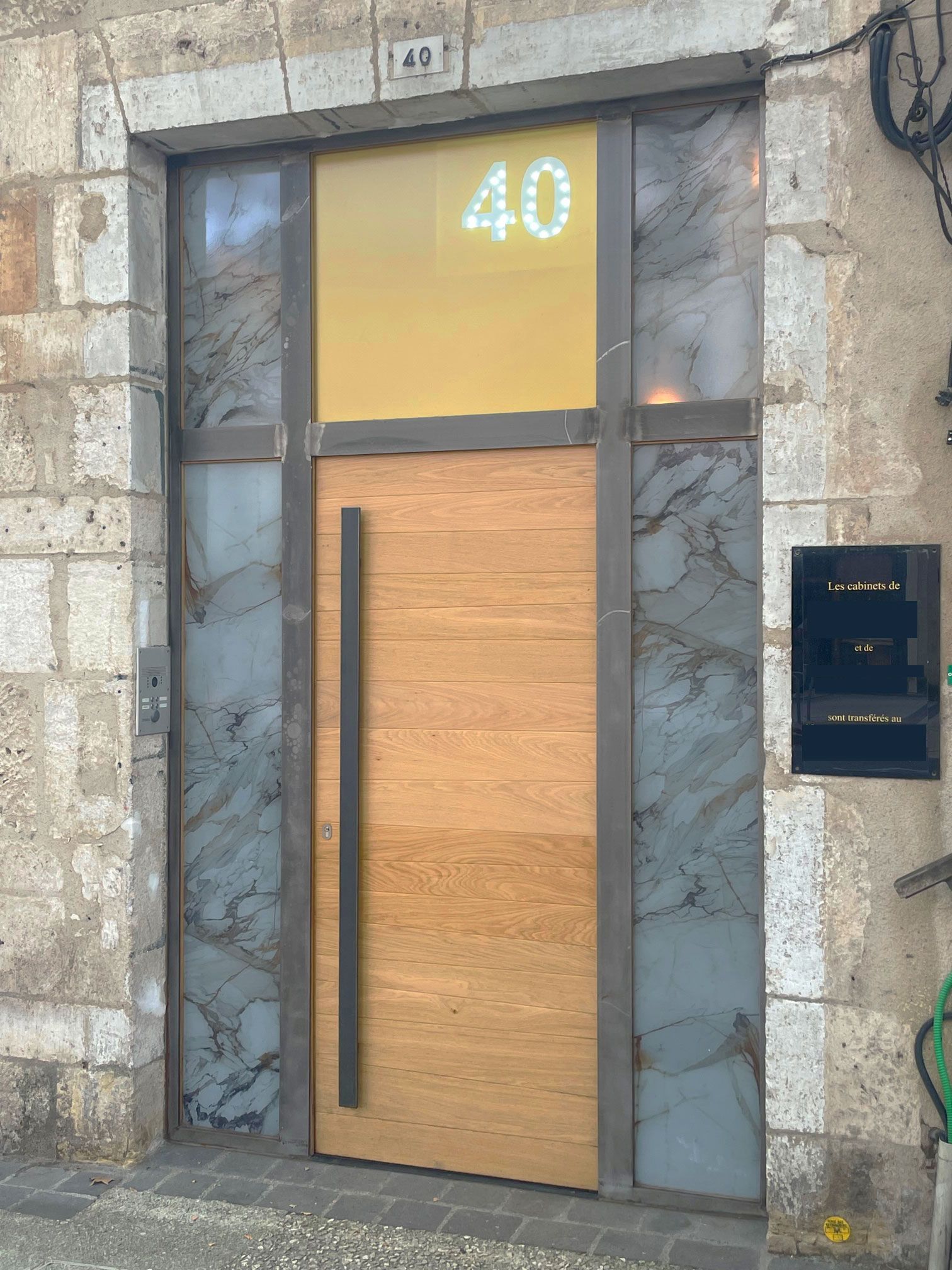 Porte en bois avec poignée verticale, numéro 40 dans une fenêtre éclairée, façade en pierre.