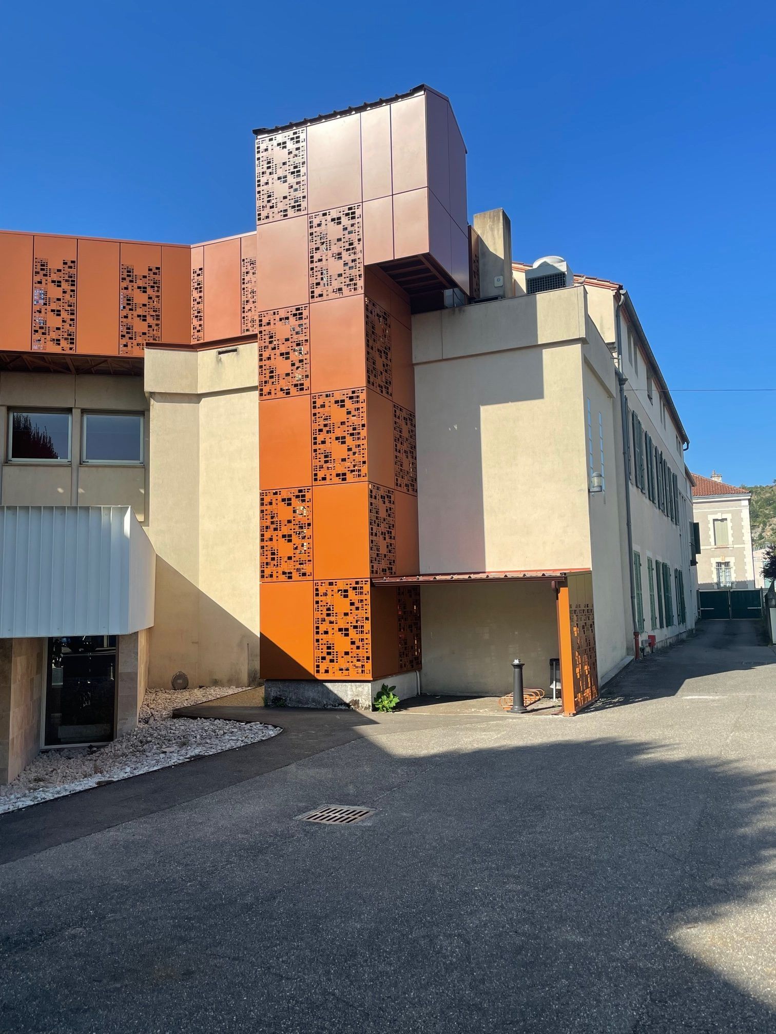 Bâtiment à façade métallique orange et panneaux perforés sous un ciel bleu.
