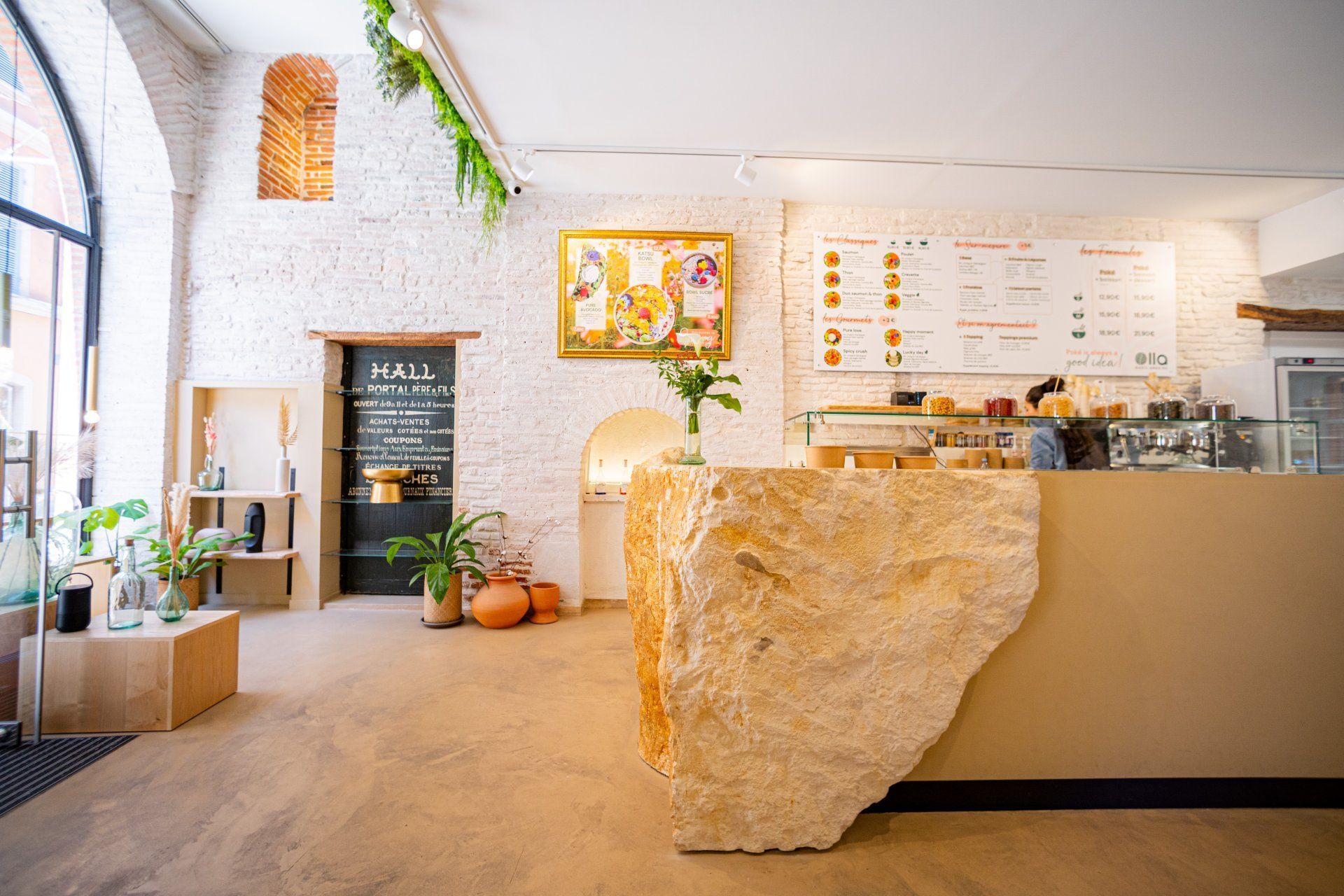 Intérieur d'un café avec un comptoir en pierre texturée, un tableau de menus et un mur de briques.