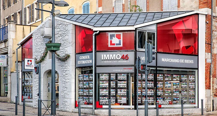 Façade de l'agence immobilière IMMO46 avec annonces de biens. Accents rouges et gris, vitrines.