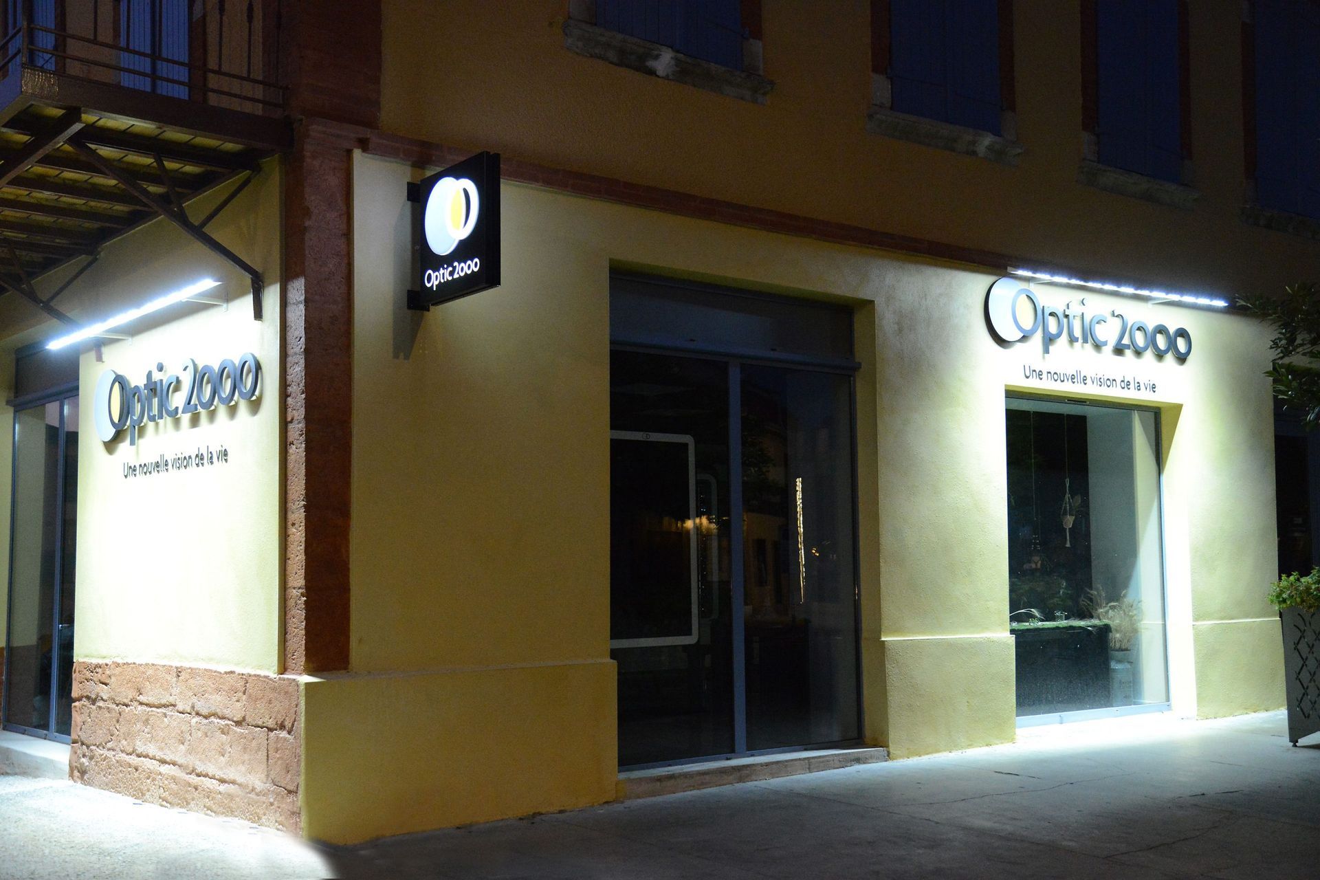 Extérieur du magasin Optic 2000 la nuit, avec son enseigne et son entrée illuminées.