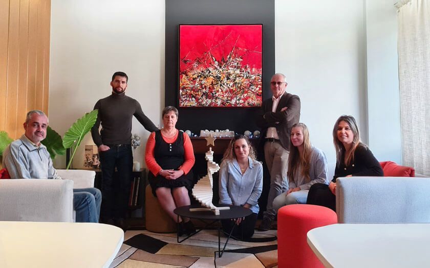 Un groupe de huit personnes assises et debout dans un salon moderne, devant une œuvre d'art abstraite rouge.