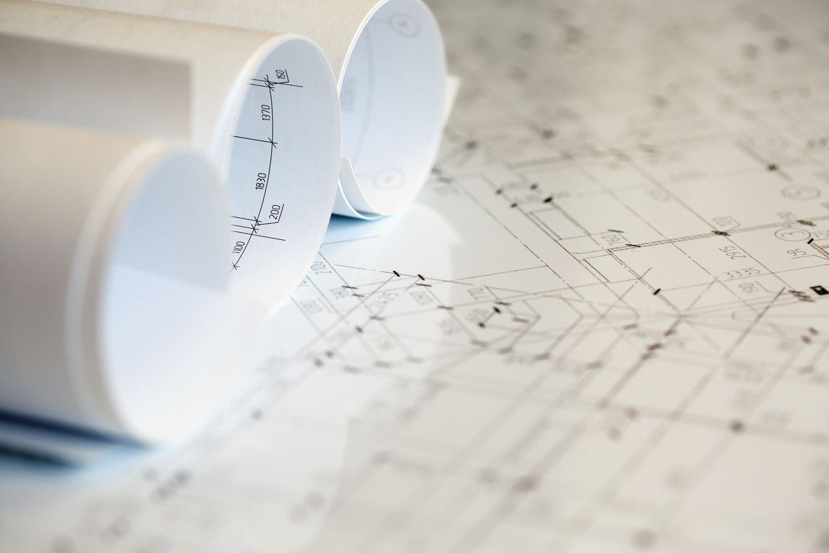 Plans architecturaux enroulés, partiellement déroulés, sur une surface réfléchissante.