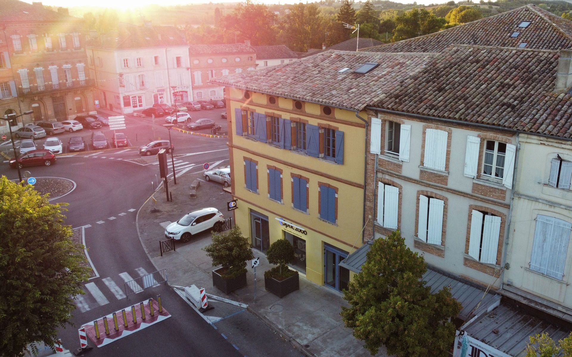 Place de la ville avec ses bâtiments, son rond-point et ses voitures garées au coucher du soleil.