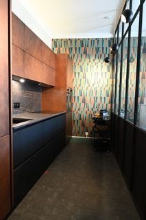 Cuisine moderne avec placards en cuivre, plans de travail noirs, mur à motifs et mur vitré.