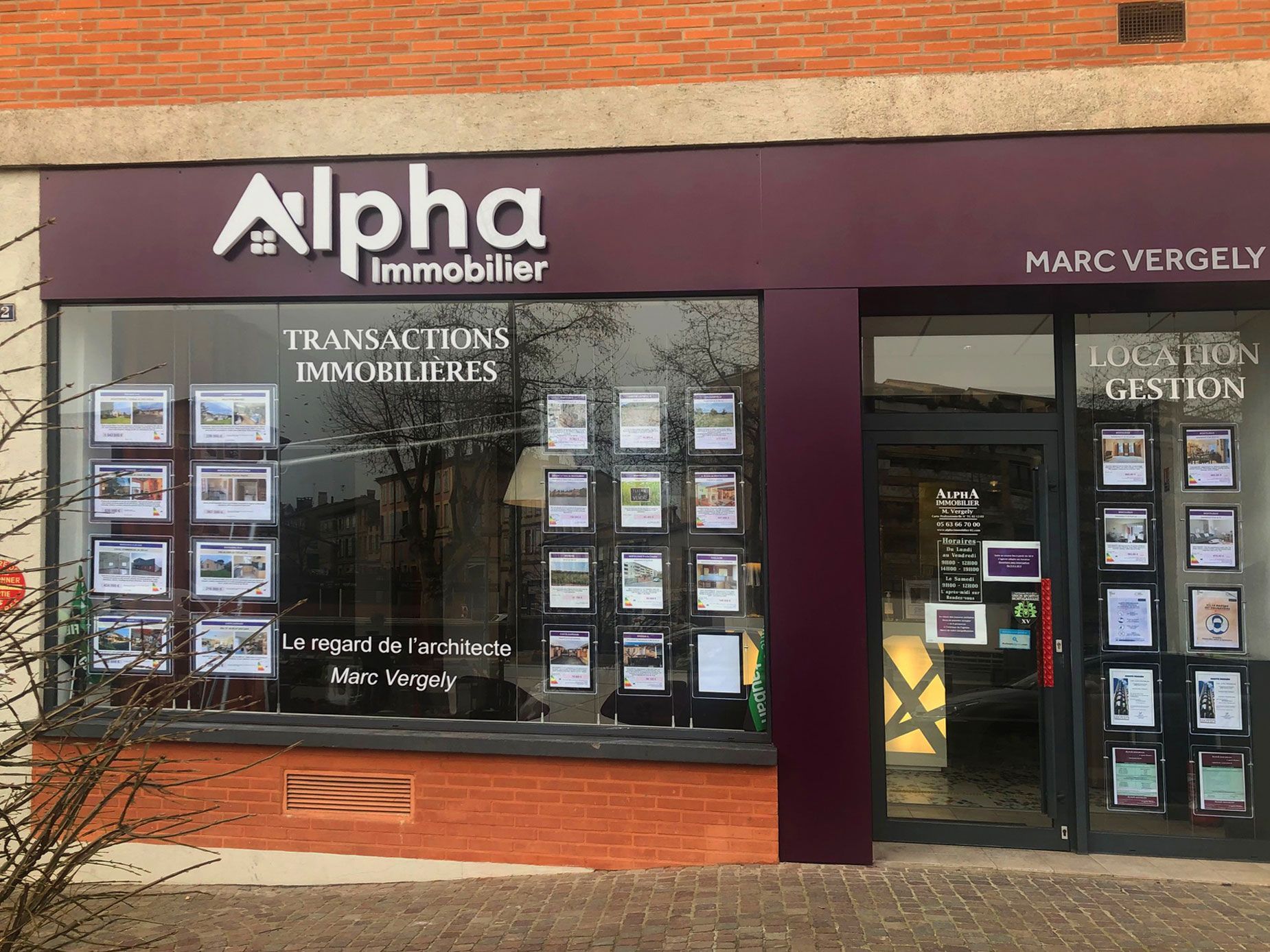 Agence immobilière avec enseigne  Alpha immobilier . La vitrine affiche les annonces immobilières.