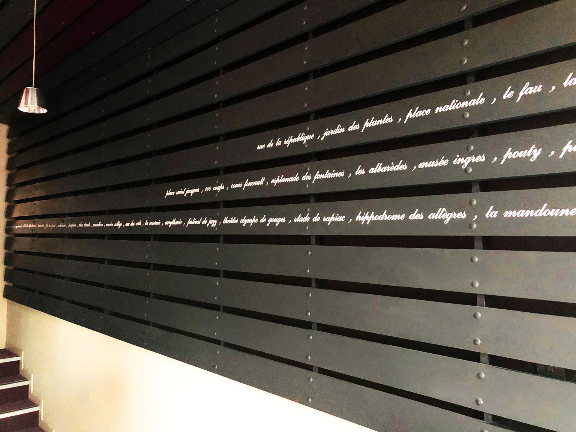 Mur sombre avec des lignes horizontales de texte en caractères blancs. Le texte est probablement en français.