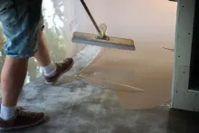 Una persona utiliza una espátula de mango largo para extender un revestimiento líquido.
