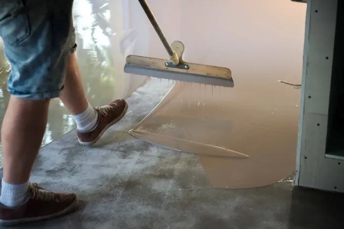 Una persona utiliza una espátula de mango largo para extender un revestimiento líquido.