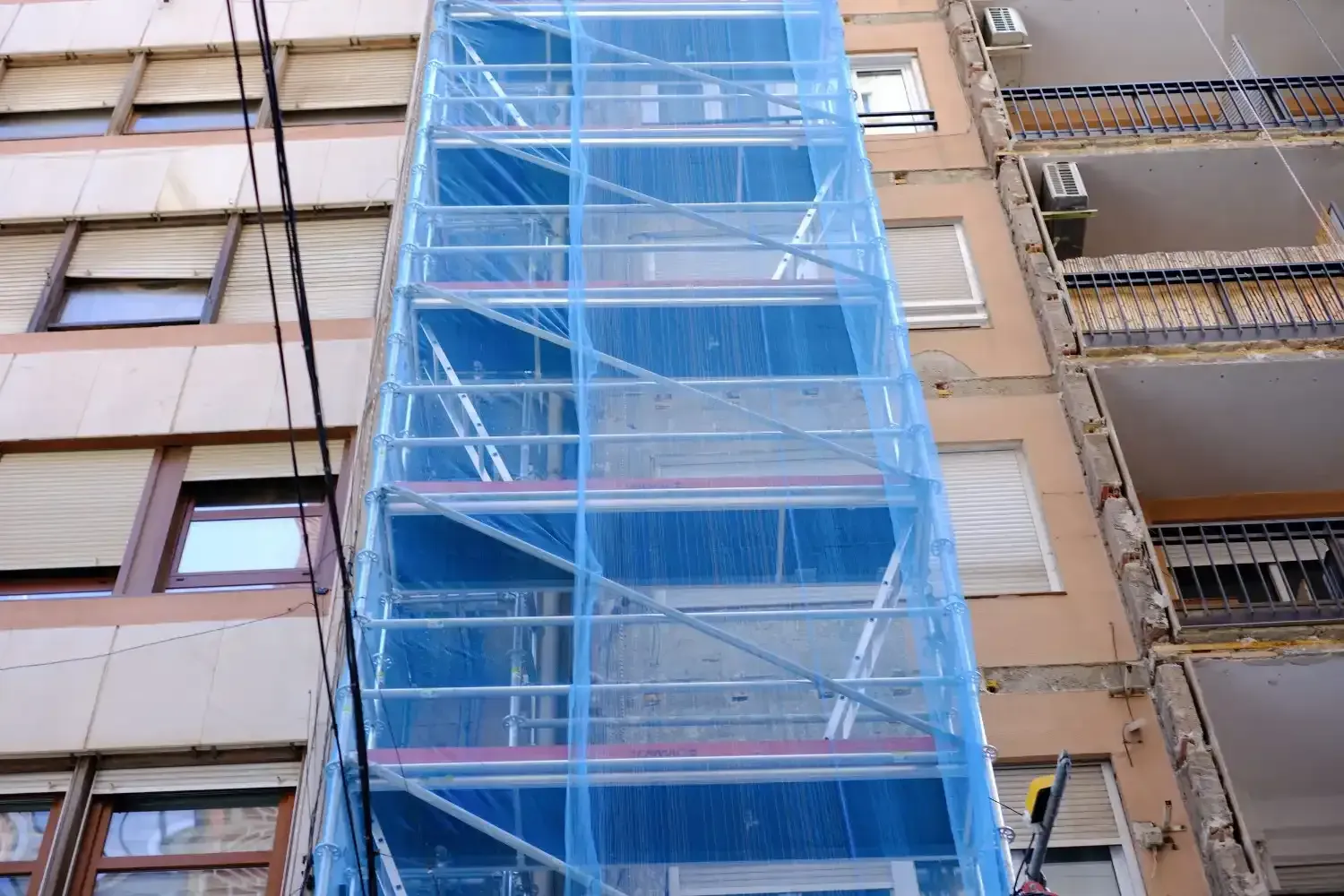 Una red de seguridad azul cubre los andamios fijados a la fachada de un edificio de apartamentos de varias plantas.