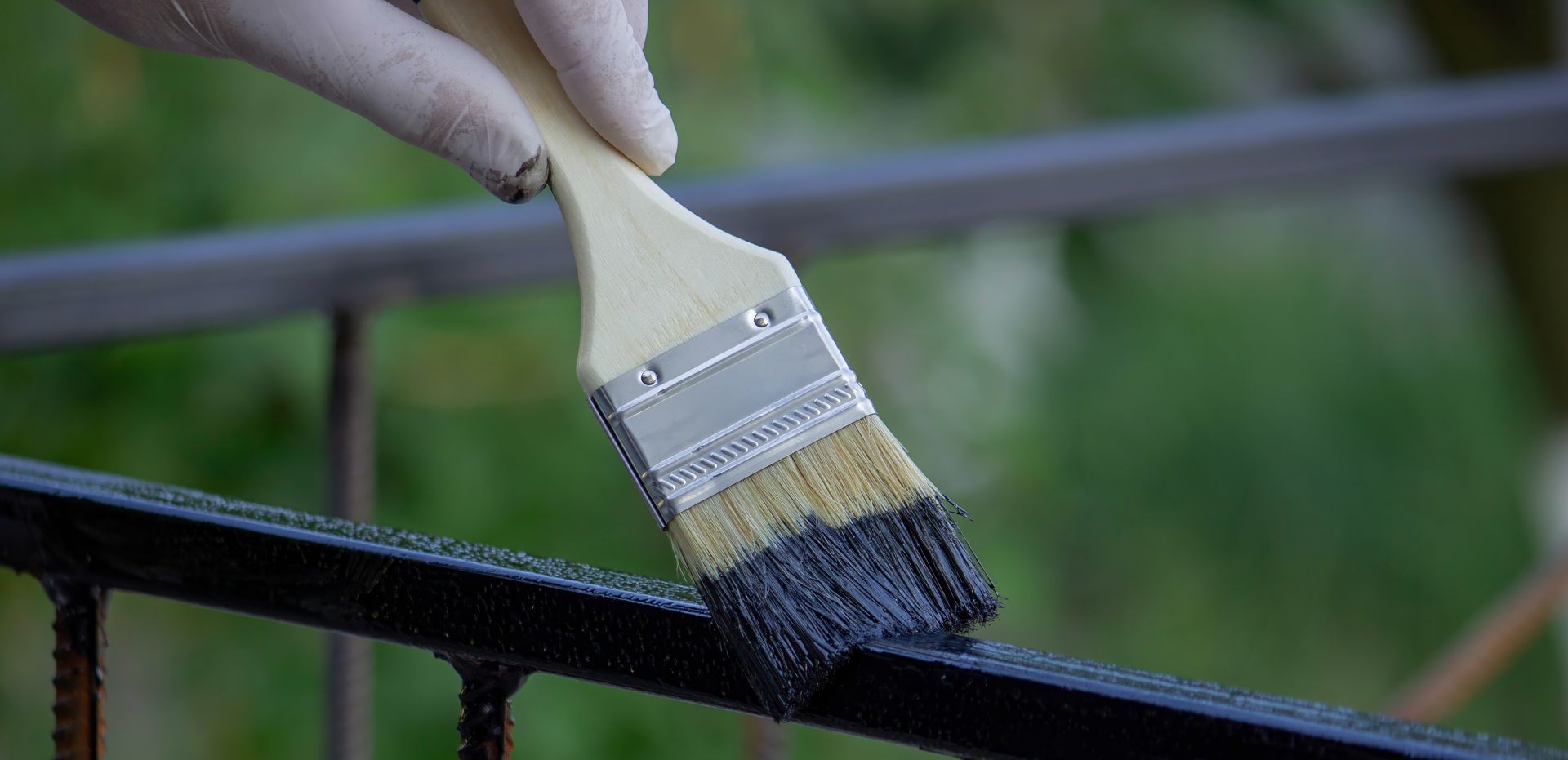 Une personne portant un gant peint une balustrade en métal noir avec un pinceau à l'extérieur.
