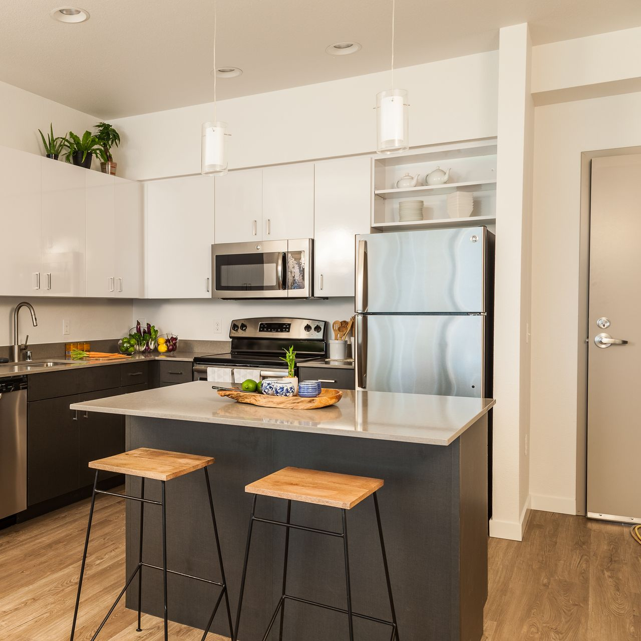 Cuisine moderne avec armoires blanches, électroménager en acier inoxydable et un îlot gris avec deux tabourets.