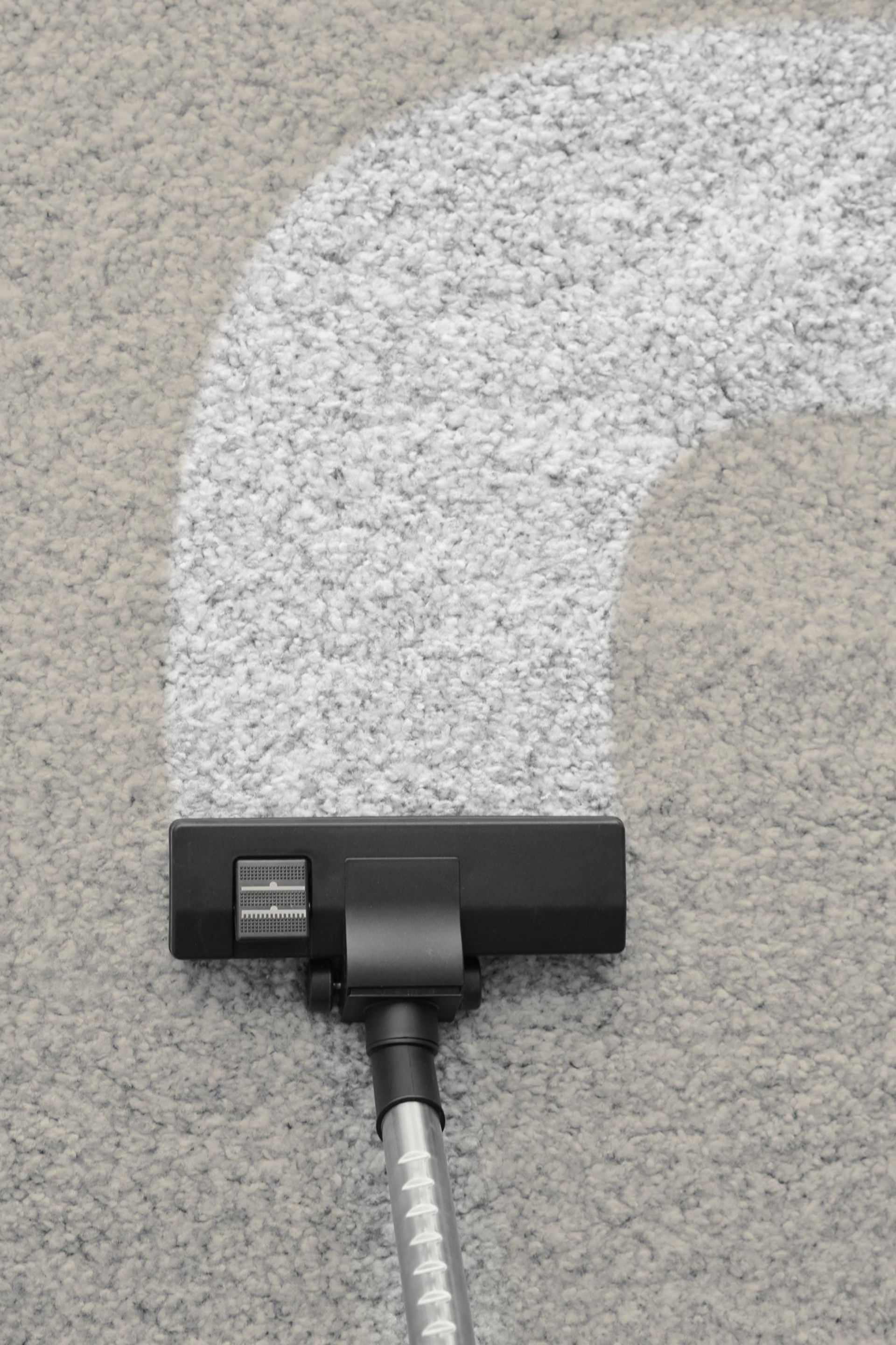 Aspirateur nettoyant un tapis gris clair, laissant un chemin blanc propre.