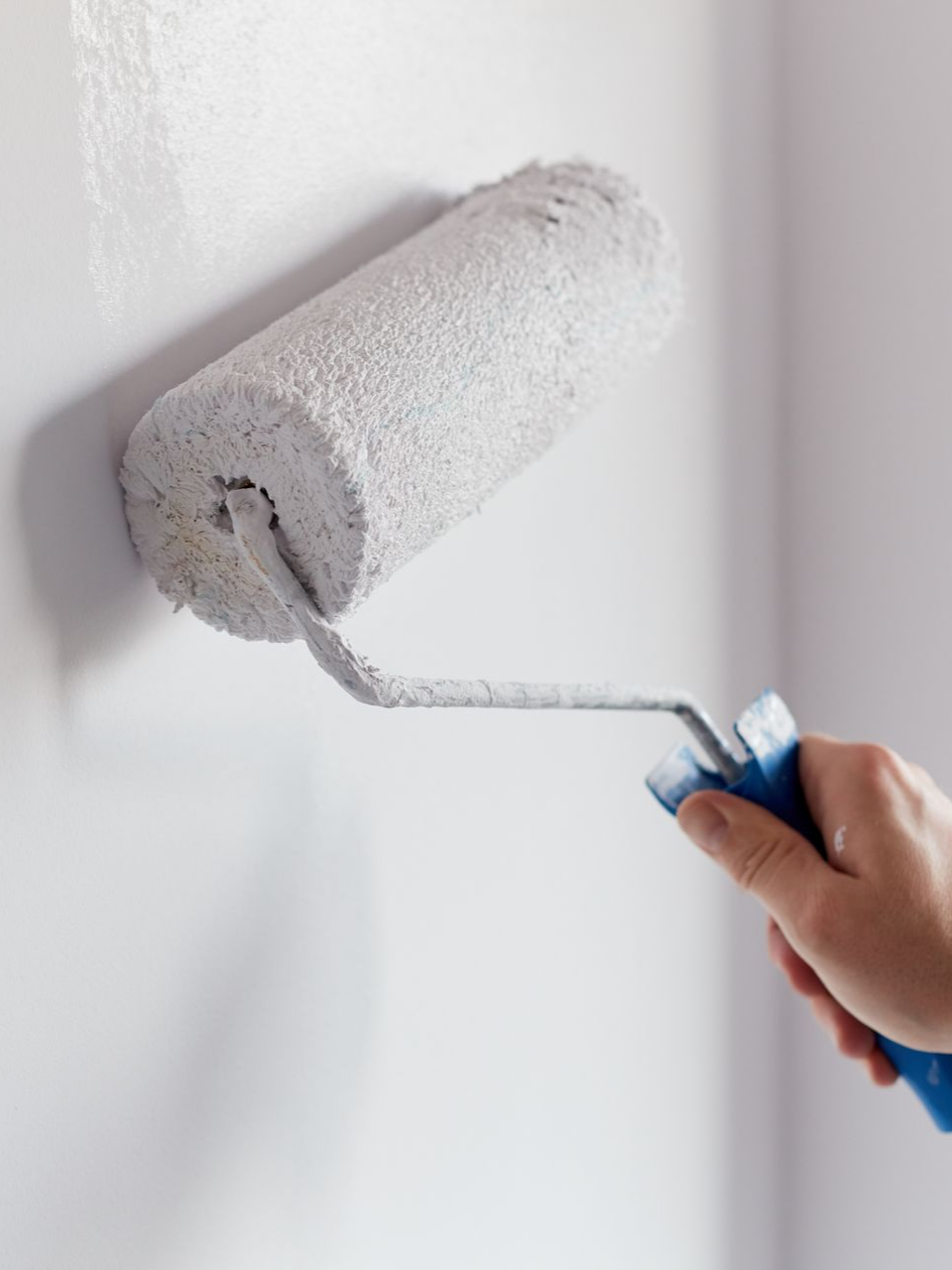 Appliquer de la peinture blanche sur un mur à la main avec un rouleau à peinture.